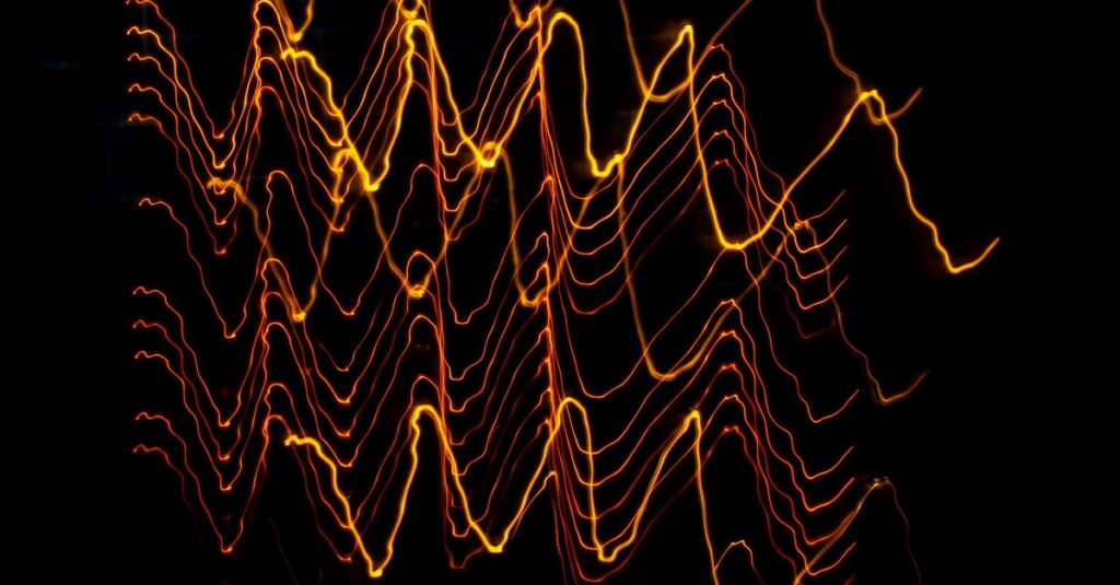 成交量vs.波動率:高手如何結合成交量(Volume)與波動率(Volatility)看懂市場趨勢? Long exposure of creative modern freezelight light painting with bright wavy lines creating patterns shining on black background in darkness